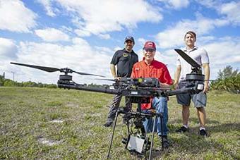 three men holding a drone