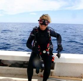 woman in scuba gear holding a fish on a boat with ocean in background